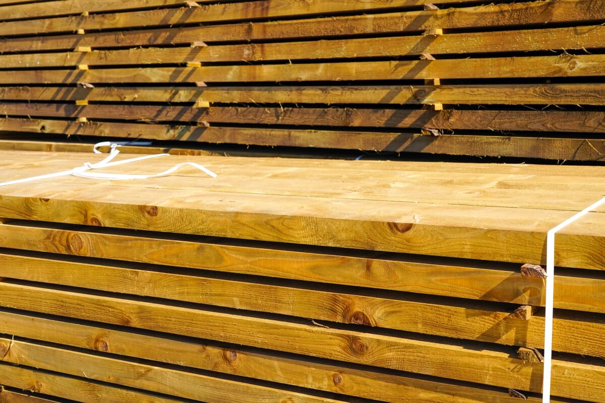 Stosy tarcicy impregnowanej ułożonej na placu składowym.